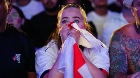 PA Una mujer sosteniendo la bandera de Inglaterra frente a su cara, luciendo sorprendida.