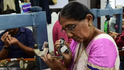 A worker wearing a pink and white saree checks a diamond at a diamond polishing workshop in Ahmedabad city. 