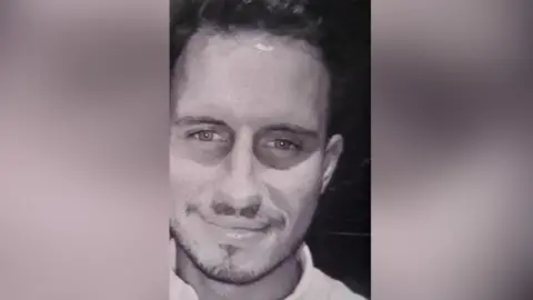 Wales News Service Jason Smith is smiling at the camera, wearing a collared shirt and has a small amount of facial hair. It is a black and white image.