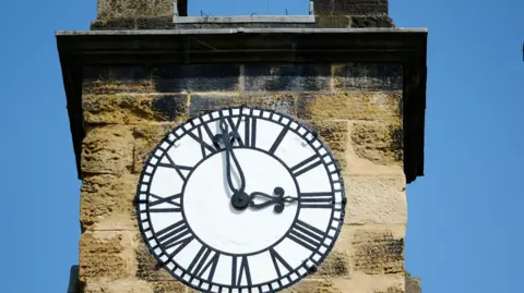 Howardian Hills/Tony Bartholomew A white clock face with black roman numerals and hands on a stone clocktower.