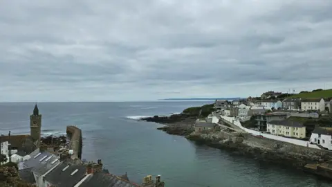 Jerry Betteridge Buildings can be seen on either side of a harbour, with a harbour wall on the left near a clock tower. The sea and sky appear calm in this photo taken by Jerry.
