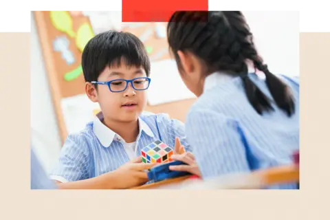 Getty Images Dua anak berseragam sekolah bermain dengan kubus puzzle berwarna-warni