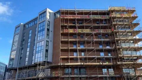 A multi-storey block of flats under construction with scaffolding erected on one side of it.