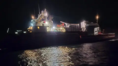 A cargo vessel that has run around - the boat is lit by various lights, with the sky pitch black.