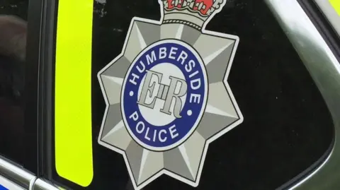 The Humberside Police logo on the side of a police car with Humberside Police in a blue circle, ER in the middle and a star and crown around it. 