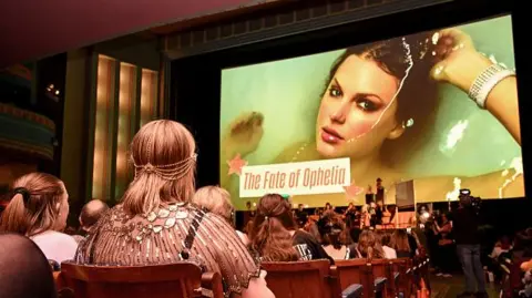 Getty Images Taylor Swift fans listen to a song during a listening event for Swift's new album 'The Life of a Showgirl' at the Astor Theatre in Melbourne on October 3, 2025. They are seated in a cinema space and some are dressed up in 1920s clothes. 