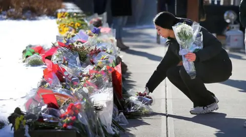 A young woman lays flowers at a memorial to victims at Brown University