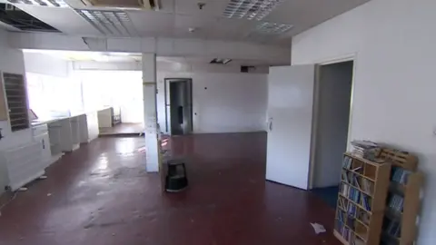 An empty office with a red floor and white walls and a couple of bookcases pushed against the wall.