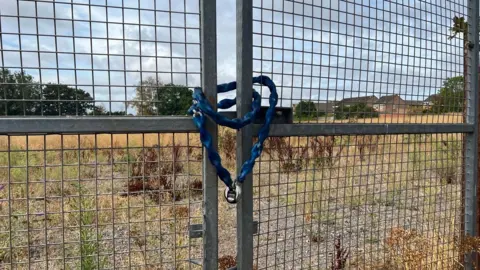 The image shows gates to the field on Ribston Avenue with a chain and padlock around them.