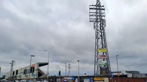 LDRS A tall flood-light stand at the corner of a football stadium, set against a rather gloomy and cloudy sky.
