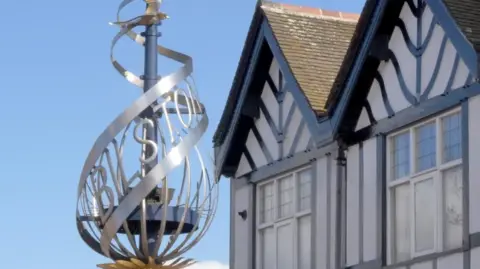 A swirling, silver sculpture spells out the name Bilston next to some black and white houses.