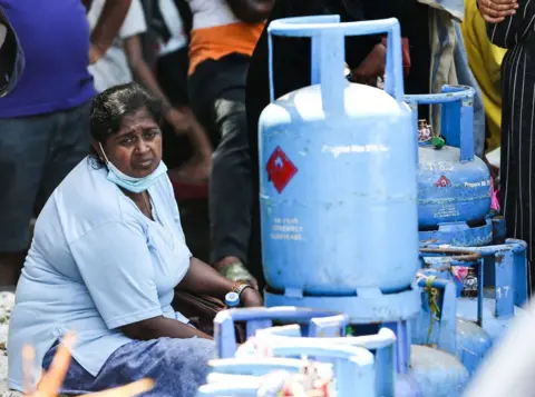 Getty Images Seorang wanita duduk di samping tumpukan tabung gas minyak cair