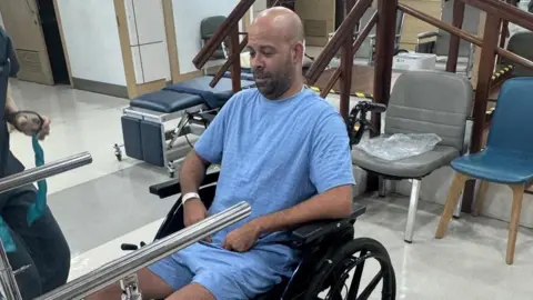 A man in a wheelchair wearing blue hospital garb.