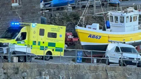 RNLI New Quay A pier with a docked yellow and balck boat, and a yellow ambulance parked up next to it.