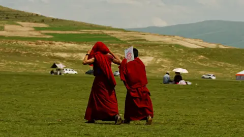 Xiqing Wang/ BBC Young monks walk pastm covering their hard from the sharp sun 
