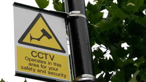 A yellow sign on a lamp-post reads: "CCTV operates in this area for your safety and security"