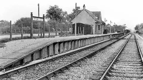 Disusedstations.org An archive black and white image of Marchwood station showing the rails and a small station building with a 'Marchwood' station sign