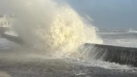JULIE SHIMMIN A wave crashes over a wall in Castletown and spills onto the road.