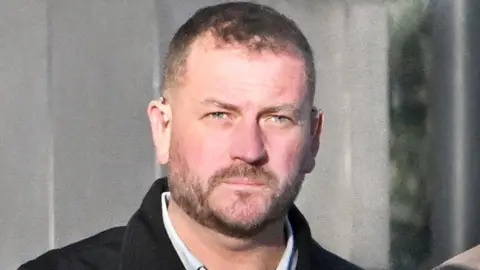 Stephen Murney is pictured outside Belfast Crown Court.He is wearing a black coat and white shirt. he has short brown hair and a short beard