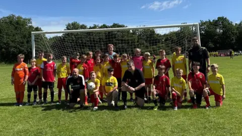 Suzanne Cook Bishops Waltham Dynamos FC, a young team of children with their adult coaches.