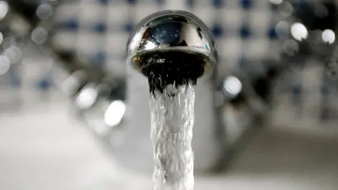 A stream of water falls out of a sliver tap. 