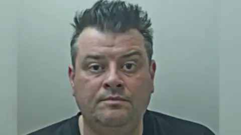 Lancashire Police Chris Higgins has spiky black hair, is clean shaven and is wearing a black T-shirt in this custody image.