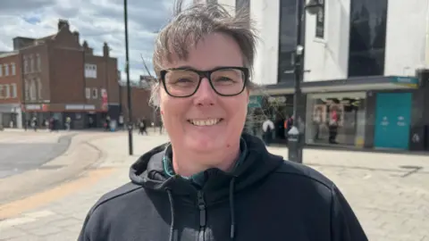 A woman with brown hair wearing black glasses and a black hoody