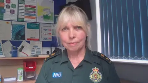 A woman with blonde hair in a green paramedic uniform looking at the camera