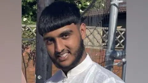 Family Zeshan Afzal pictured in a white Thawb smiling. He has thick black hair and a beard.

