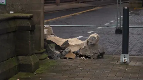 A pile of rubble lies on a cobble street next to Hull Minster. A metal fence has cordoned the area off and is visible in the background.