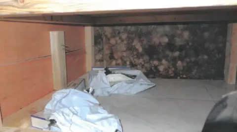 City of Wolverhampton Council Cigarettes wrapped in white plastic in a storage area of a shop. They are hidden away with a wooden wall next to them and are sat on white tiles.