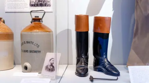 Stephanie Belton A display case with ceramic beer pots and Victorian boots in it.