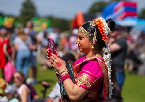 Gary Cantwell A woman in bright pink traditional clothing looks at her phone, with people in the background 