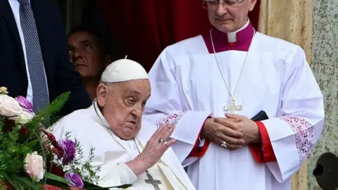 Getty Images The Pope on his last public appearance on Easter Sunday, waving while a member of the clergy watches on.