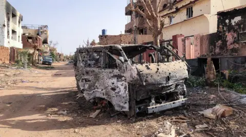 AFP This picture taken on May 30, 2024, shows a burnt vehicle in front of damaged shop in Omdurman