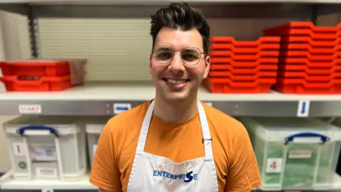 Alex Bird from Enterprise Packaging in front of a shelf containing components for the retrieval kits