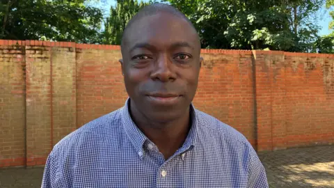 Matt Knight/BBC A man with a smart checkered-shirt and a wall in the background