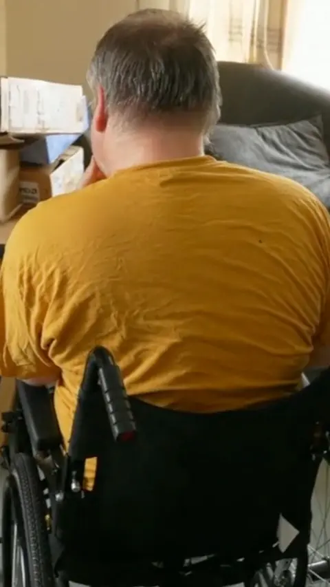 A man in a yellow top and in a wheelchair with his back to the camera.