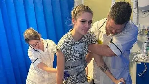 Freya Theobold is in hospital and being supported by two medical staff as she moves around. She has a brace over her body.