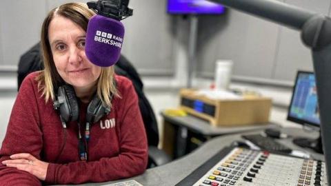 Sarah Walker sat in front of a radio desk and a microphone, which has a BBC Radio Berkshire muff on it