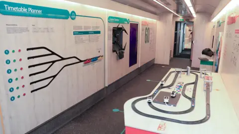 Phil Marsh The interior of a train carriage which has been converted to house an interactive exhibition featuring a model train track and an interactive "timetable planner" among other displays. 