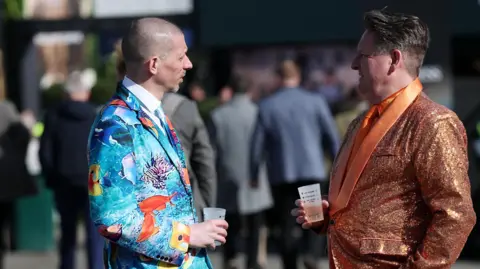 Reuters Two men face each other as they chat while holding drinks. One has a shiny orange formal suit on, while the other is wearing a light blue suit with colourful emblems on it