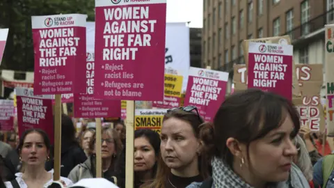 EPA A close-up shot of female counter protesters. They are holding pink placards that read 'women against the far right' followed by bullet points which say 'reject racist lines' and 'refugees are not to blame'.