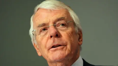 Sir John Major appears on a green-grey background