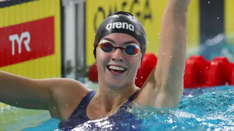 Swimmer Emily Barclay smiles and waves after a race