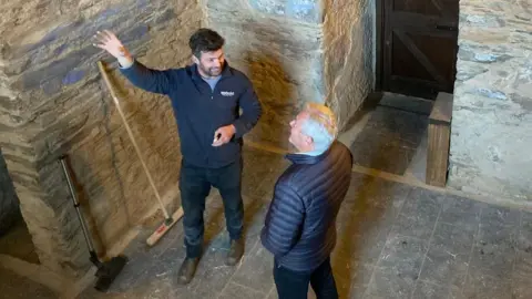 Two men, Ryan Byrne and Neil Doherty, are standing inside the fort.
One is gesturing upwards with his hand while the other follows his direction.
Both men are wearing navy coats and jackets.