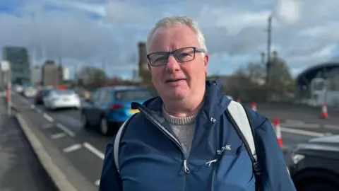 Dave Paxton wearing a jacket stands at the entrance to the Tyne Bridge 