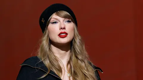 Getty Image Taylor Swift está sonriendo con un sombrero Biani negro y una chaqueta negra.
