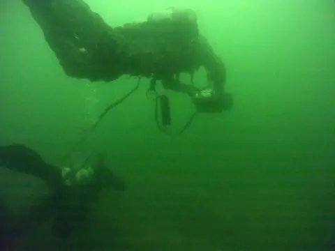 Ukrainian Navy Two members of the team diving to look for mines. The underwater image is a vivid shade of green.