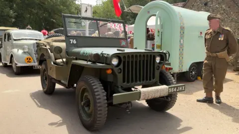 Veteran in uniform standing by a military jeep and a classic car.